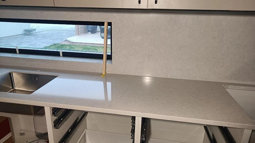 Polerad Silestone Snowy Ibiza med rostfri diskho, låg fönsterlinje och matchande väggpanel i ett kök i Skurup.