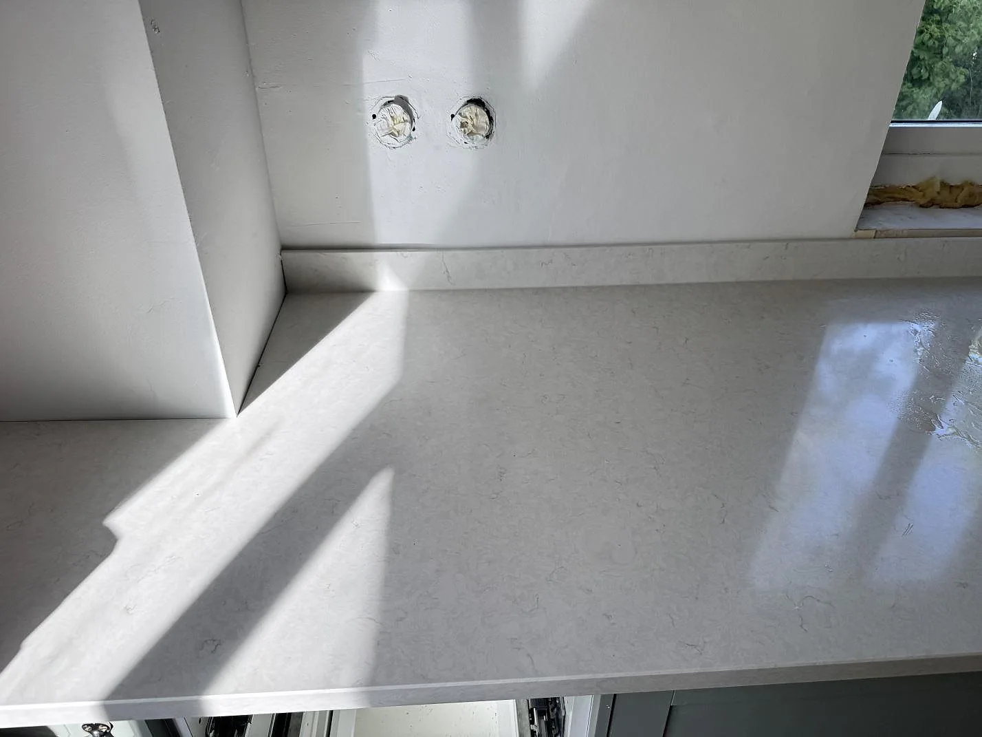 Polerad Silestone Snowy Ibiza i kvartskomposit som lång köksbänkskiva under fönster, med låg stänkkant och öppna stommar i Smygehamn.