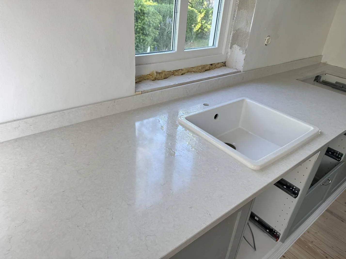 Närbild av polerad Silestone Snowy Ibiza som köksbänkskiva i kvartskomposit med vit diskho, låg stänkkant och fönsterparti i Smygehamn.