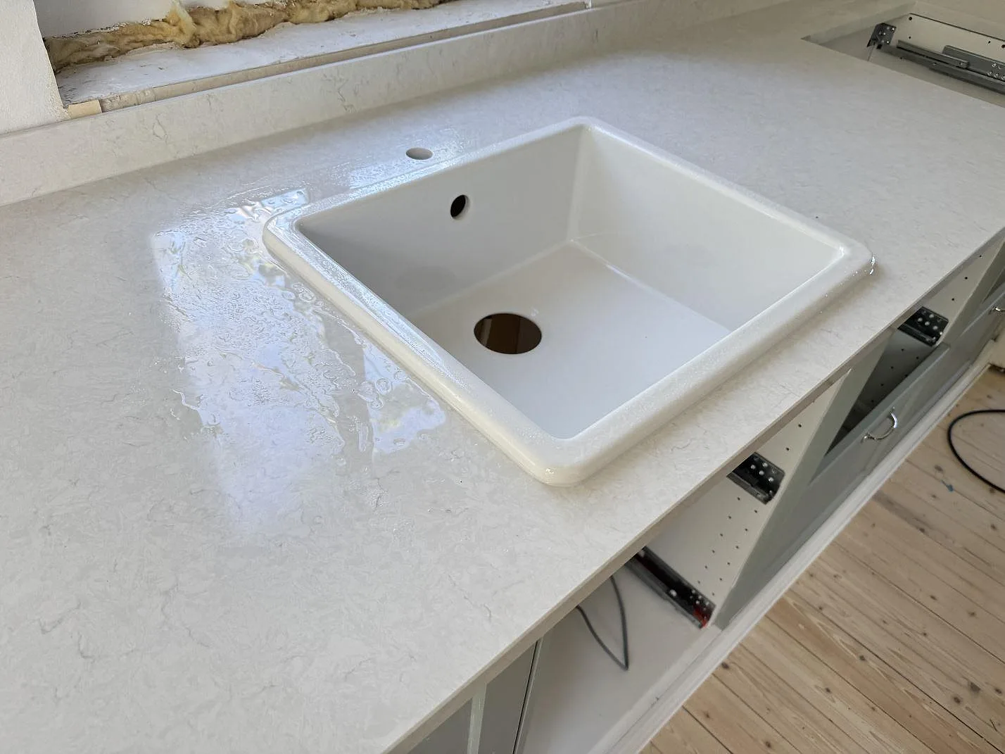 Detaljbild av vit diskho och polerad Silestone Snowy Ibiza i kvartskomposit i ett kök under montering i Smygehamn.
