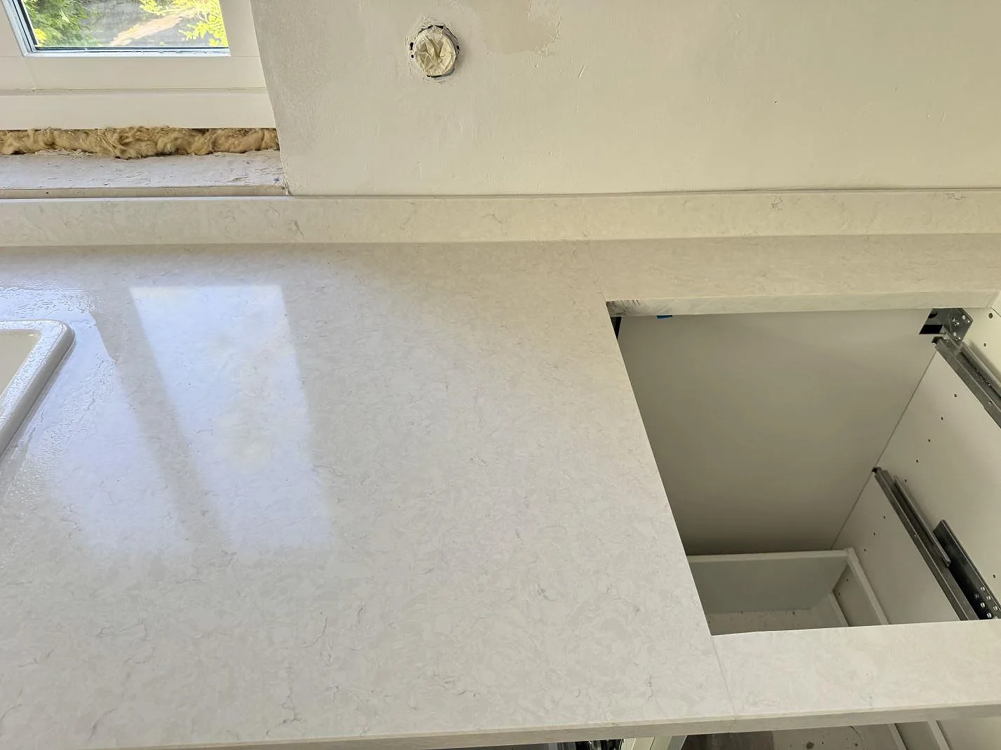 Köksbänkskiva i polerad Silestone Snowy Ibiza, kvartskomposit med ljus ådring, stänkkant och öppning i skivan i Smygehamn.