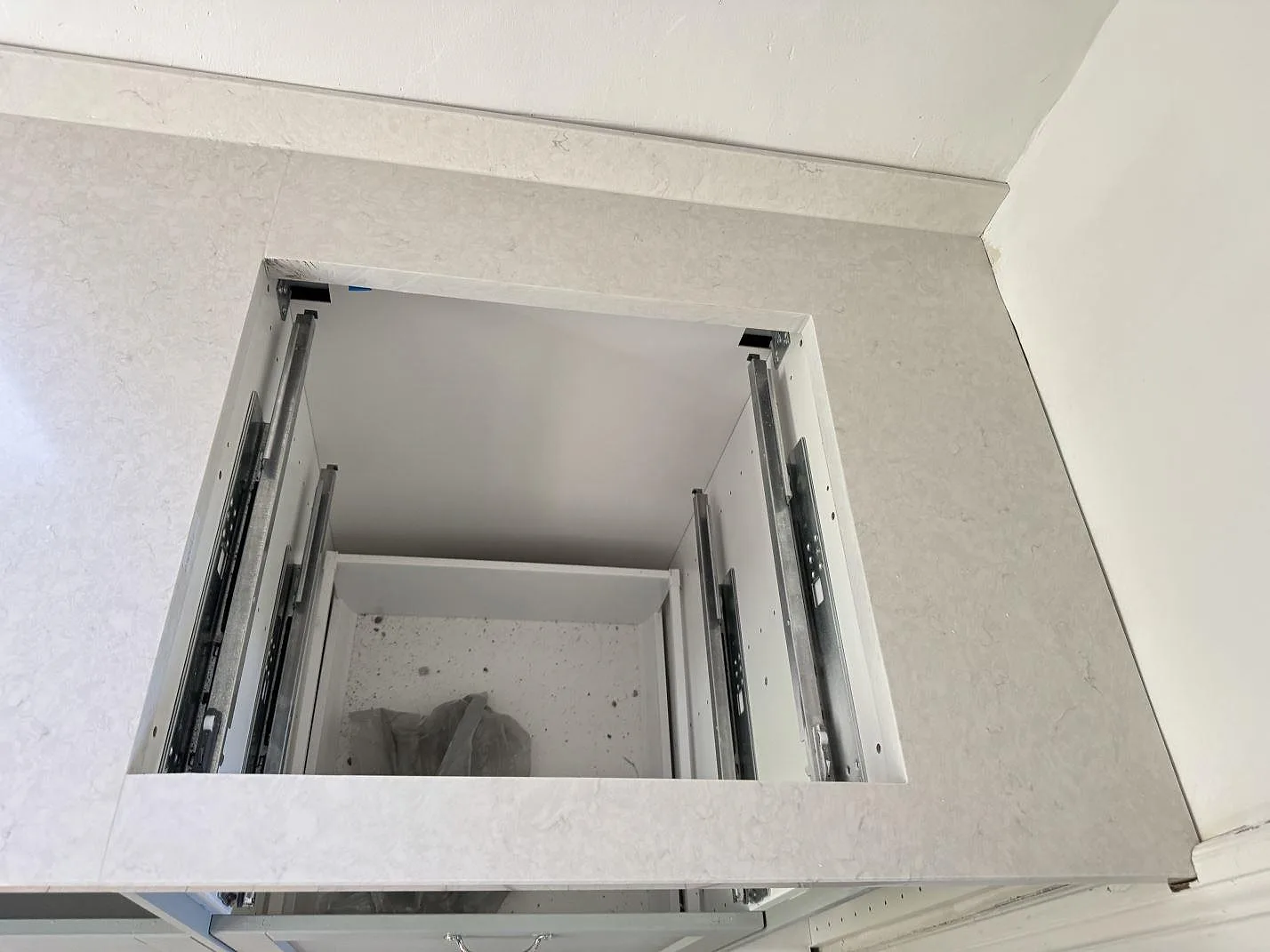 Detalj av polerad Silestone Snowy Ibiza i kvartskomposit runt skivöppning och öppna köksstommar under montering i Smygehamn.