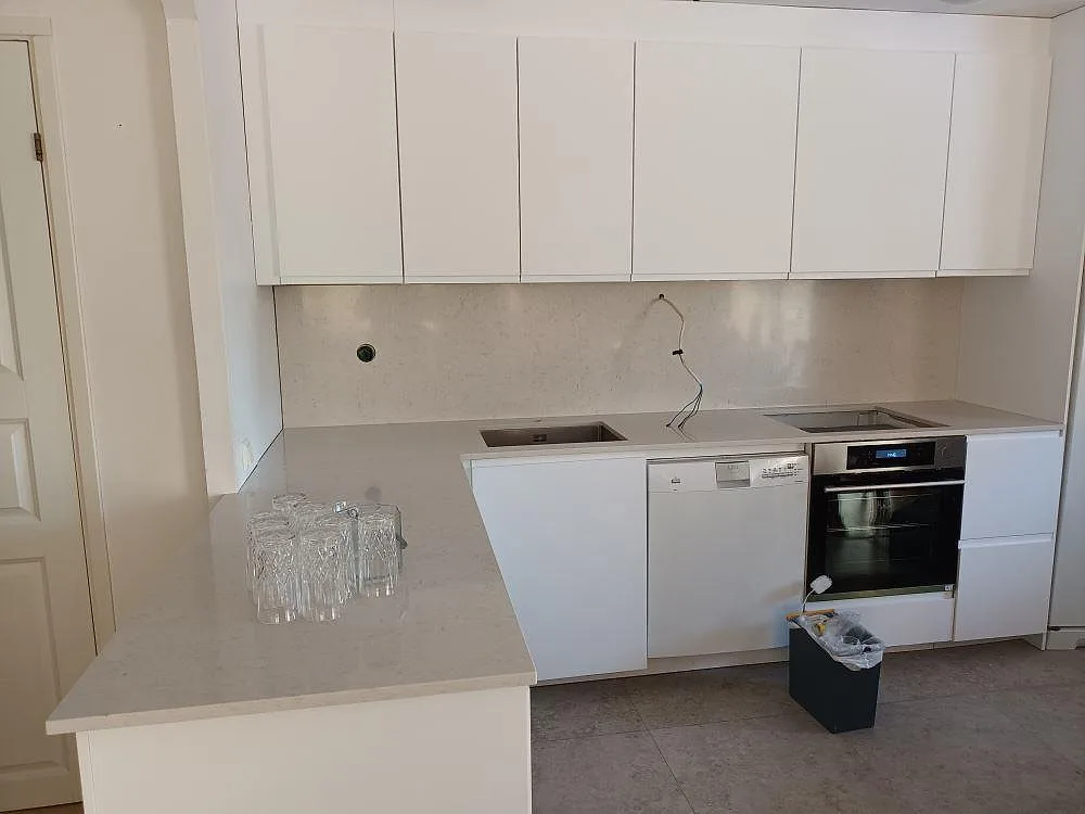 Polerad Silestone Snowy Ibiza köksbänkskiva med lågt uppvikt stänkskydd och underlimmad diskho, fotograferad under montering i ett kök i Sollentuna.