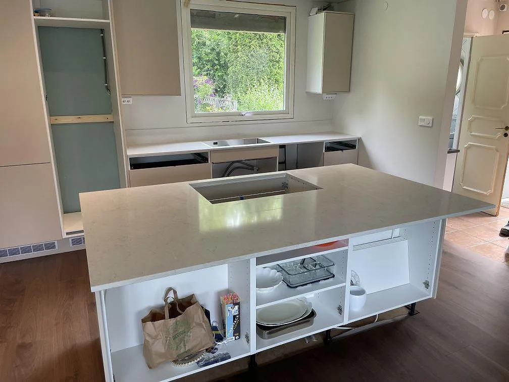 Närmare vy av köksö i polerad Silestone Snowy Ibiza med ljus ådring och öppna köksstommar under montering i Sollentuna.