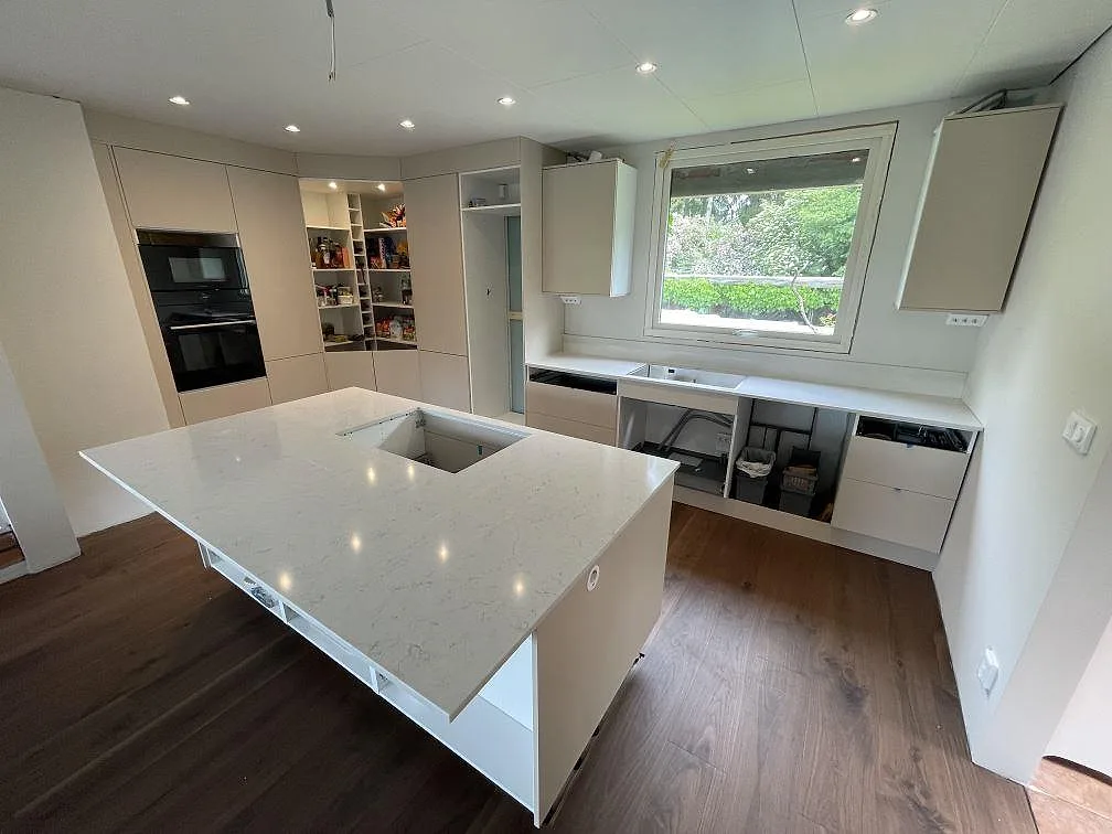 Köksbänkskiva och köksö i polerad Silestone Snowy Ibiza, vit kvartskomposit med mjuk ådring och låg stänkkant, i ett kök under montering i Sollentuna.