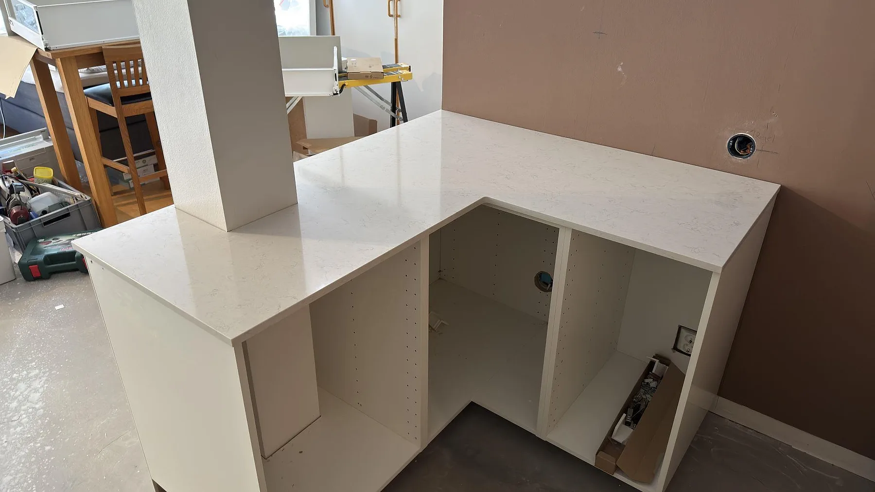 Polerad Silestone Snowy Ibiza köksbänkskiva som returyta runt en pelare, vit kvartskomposit med diskret grå ådring i ett kök under montering i Solna.