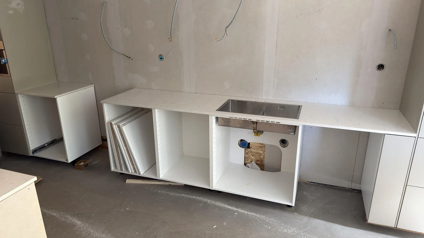 Köksbänkskiva i vit Silestone Snowy Ibiza, polerad kvartskomposit, med rostfri diskho över öppna köksstommar under montering i Solna.