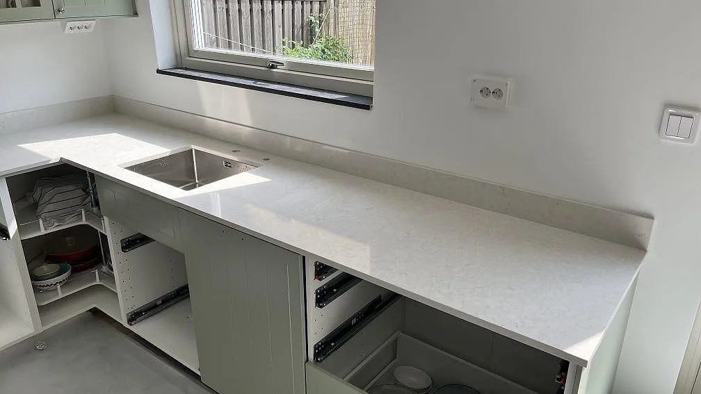 Polerad köksbänkskiva i Silestone Snowy Ibiza med diskho under fönster och låg stänkkant i ett kök i Spånga.