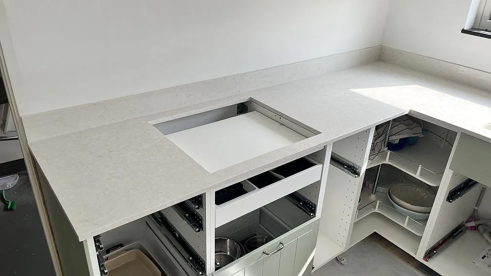 Köksbänkskiva i Silestone Snowy Ibiza, polerad kvartskomposit, med hällöppning och uppvikt stänkskydd under montering i Spånga.