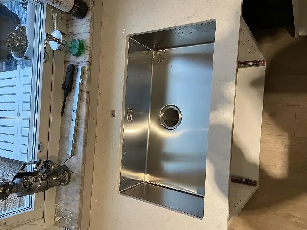 Diskbänksyta i polerad Silestone Snowy Ibiza komposit med synlig rostfri diskho vid fönster i ett kök i Staffanstorp.