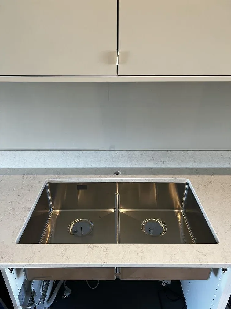 Underlimmad rostfri dubbeldiskho i en köksbänkskiva av vit polerad Silestone Snowy Ibiza i ett kök i Staffanstorp.