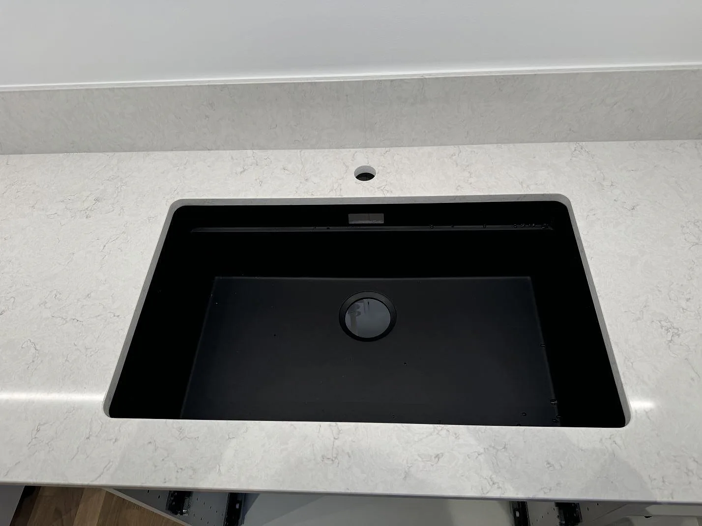 Närbild av svart diskho i polerad Silestone Snowy Ibiza bänkskiva med blandarhål och stänkkant i kök i Staffanstorp.