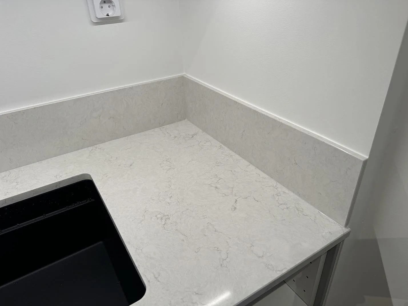Hörndel av polerad Silestone Snowy Ibiza köksbänkskiva med uppvikt stenkant och synlig svart diskho i Staffanstorp.