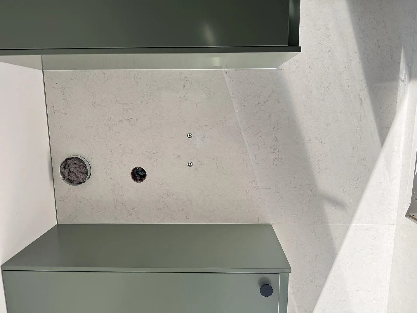 Polerad Silestone Snowy Ibiza som väggbeklädnad och bänkyta med borrade hål framför ljusgröna köksstommar i Staffanstorp.