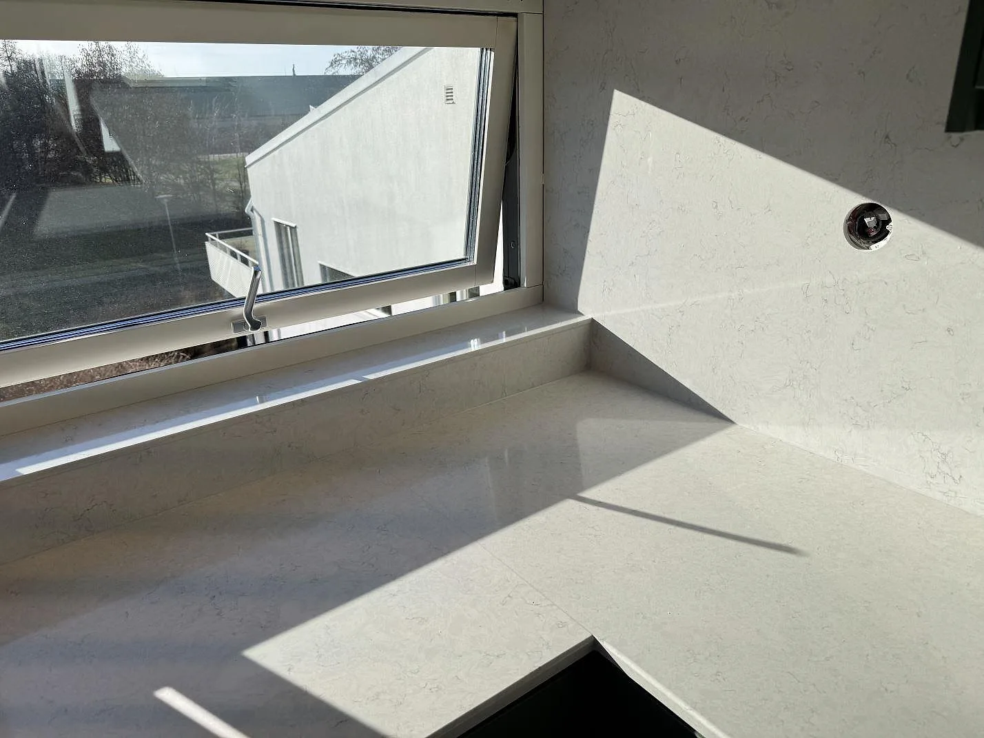 Köksbänkskiva och fönsterbänk i polerad Silestone Snowy Ibiza vid öppet fönster och ljus stenvägg i Staffanstorp.