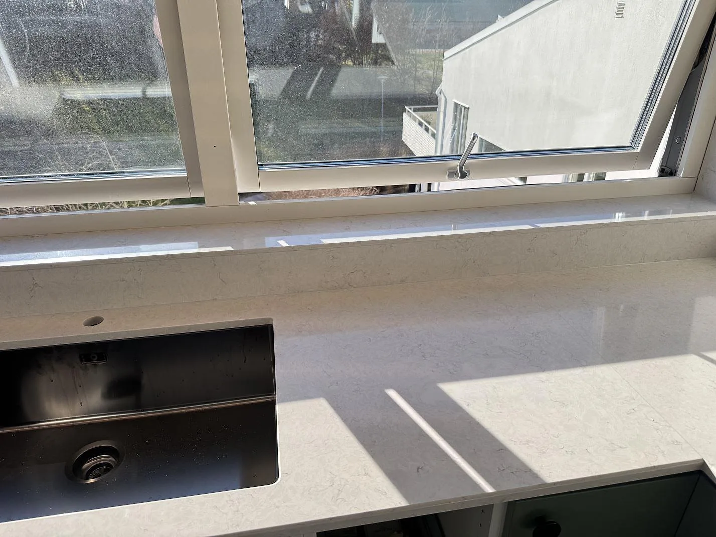Polerad Silestone Snowy Ibiza köksbänkskiva med mörk diskho och fönsterbänk vid köksfönster i Staffanstorp.
