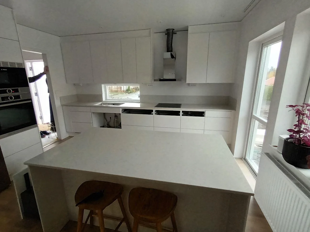 Köksbänkskiva och köksö i polerad Silestone Snowy Ibiza komposit i ett ljust kök i Stallarholmen, med diskho vid fönstret och låg stänkkant.