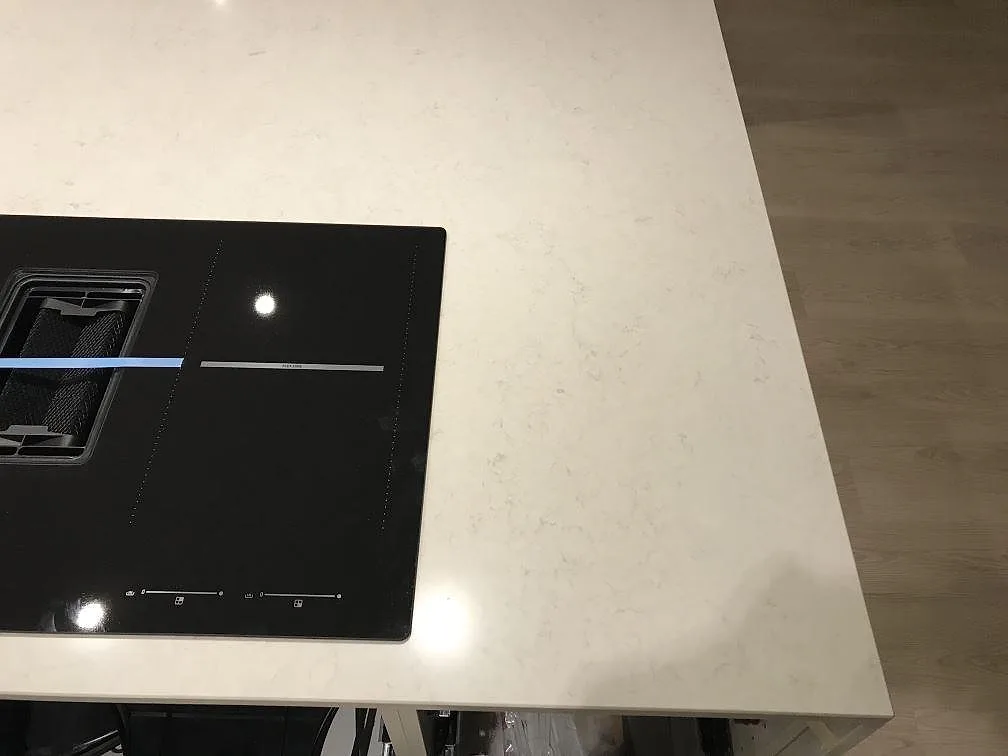 Nedsänkt induktionshäll med integrerad fläkt i en bänkskiva av polerad vit Silestone Snowy Ibiza i ett kök i Steninge.
