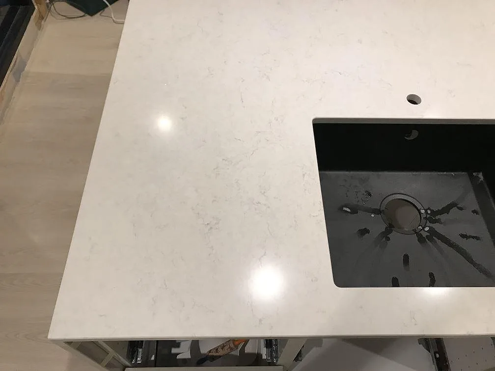 Underlimmad svart kompositdiskho i en köksbänkskiva av polerad Silestone Snowy Ibiza i Steninge.