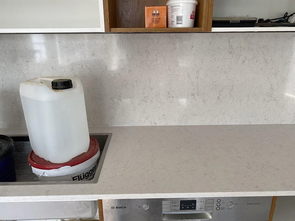 Köksbänkskiva i polerad Silestone Snowy Ibiza med urtag för diskho intill en diskmaskin, fotograferad under montering i Steninge.