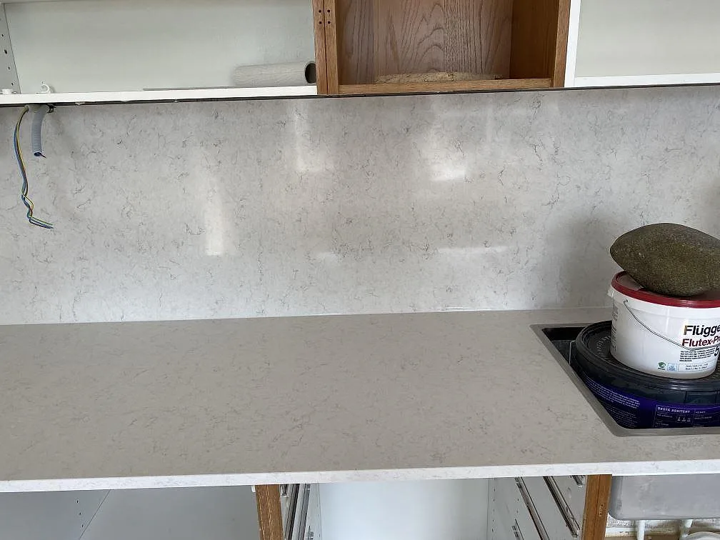 Bänkskiva och uppdragen väggbeklädnad i Silestone Snowy Ibiza med urtag, polerad yta, i ett kök under montering i Steninge.