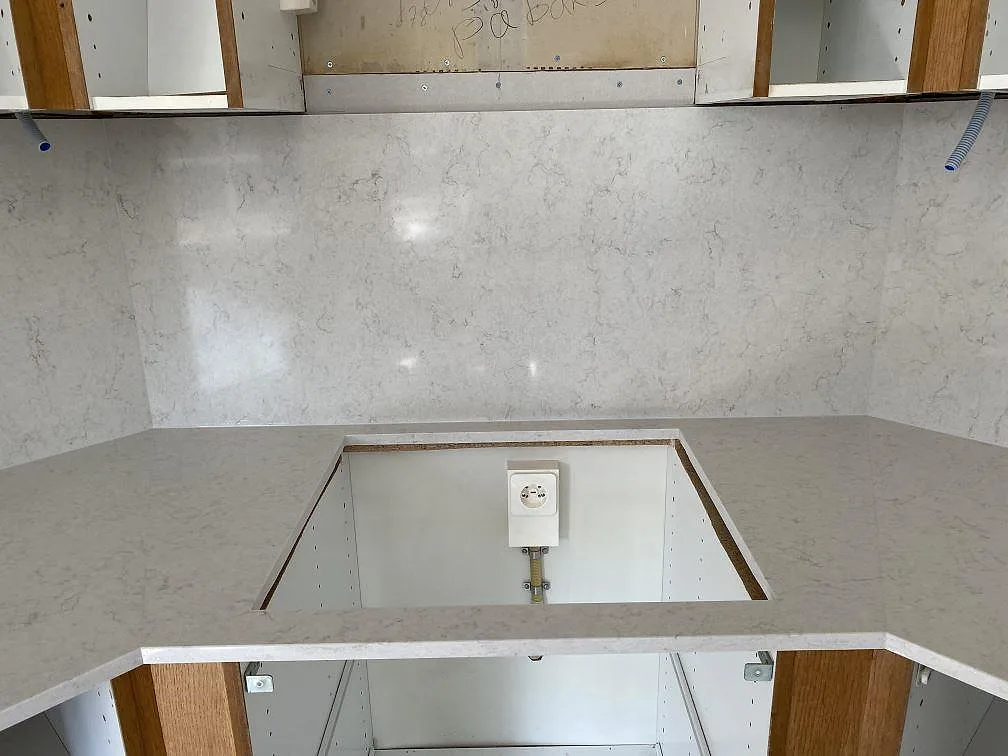 Hörnbänkskiva i Silestone Snowy Ibiza med urtag för häll och polerad väggbeklädnad i ett kök under montering i Steninge.