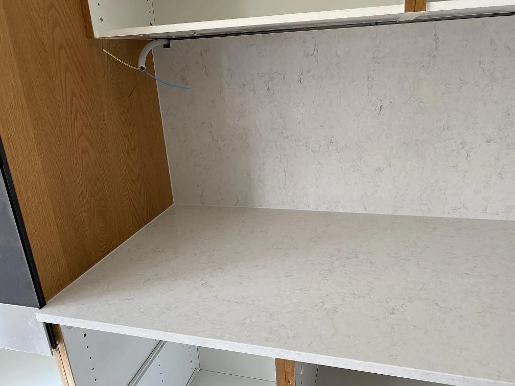 Polerad hörnbänkskiva i Silestone Snowy Ibiza med vit ådrad sten och uppdragen väggbeklädnad i ett kök i Steninge.