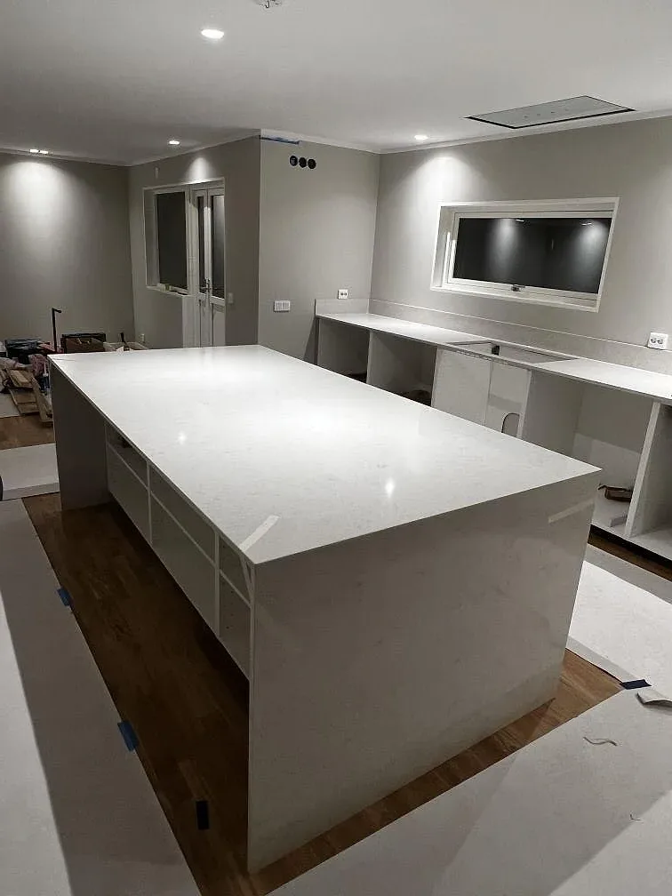 Köksbänkskiva och köksö i vit Silestone Snowy Ibiza, polerad, i ett ljust kök under montering i Stoby.