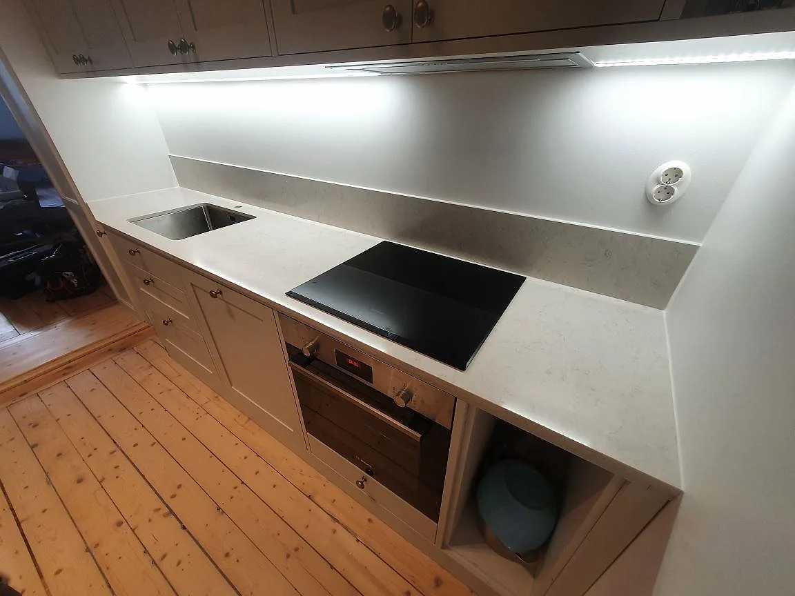 Köksbänkskiva i polerad Silestone Snowy Ibiza med låg stänkkant, rostfri diskho och svart häll i ett kök i Stockholm.