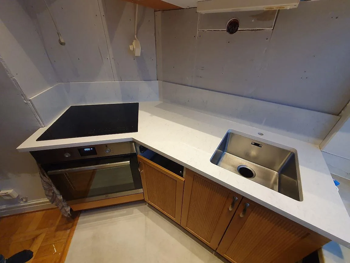 Vit Silestone Snowy Ibiza köksbänkskiva i vinkel med rostfri underlimmad diskho och induktionshäll under montering i Stockholm.