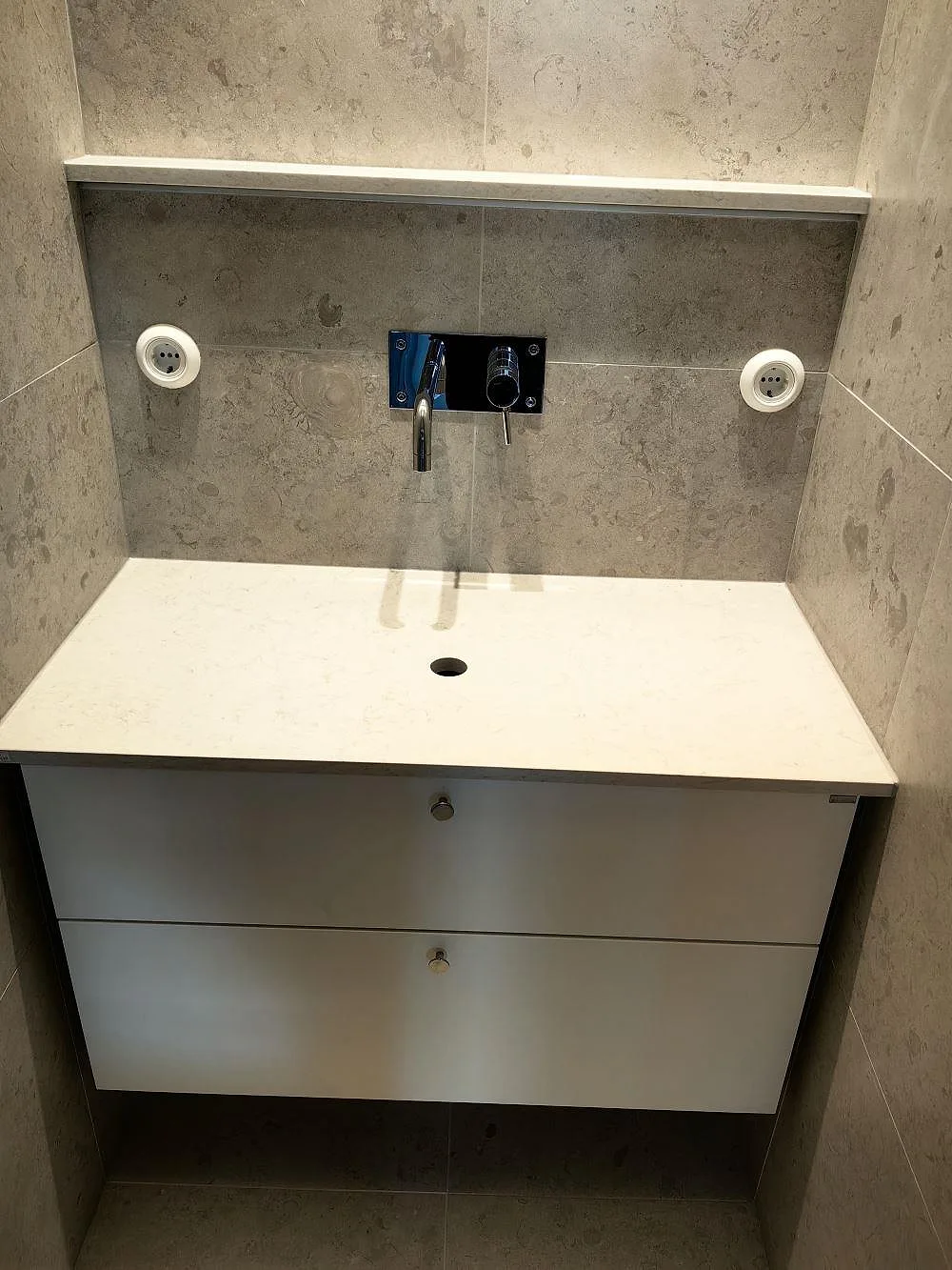 Badrumsbänkskiva i vit Silestone Snowy Ibiza, polerad kvartskomposit, på en kommod med väggmonterad blandare i Stockholm.