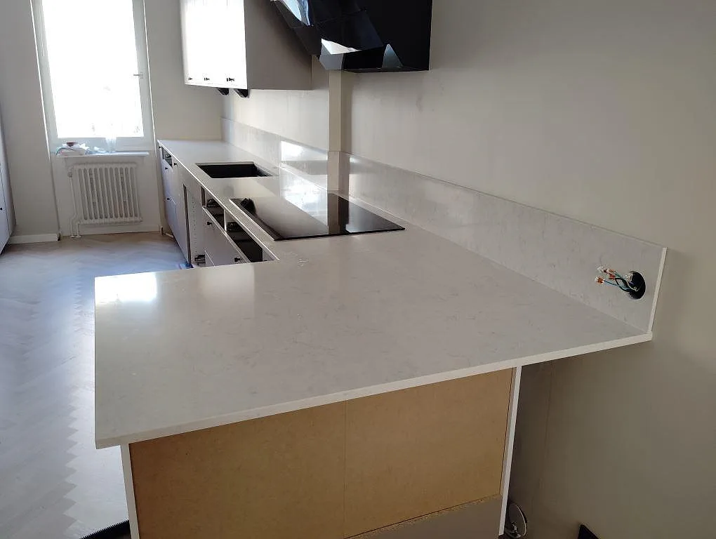 Köksbänkskiva i vit Silestone Snowy Ibiza, polerad kvartskomposit, med halvö och stänkskydd i ett kök i Stockholm.