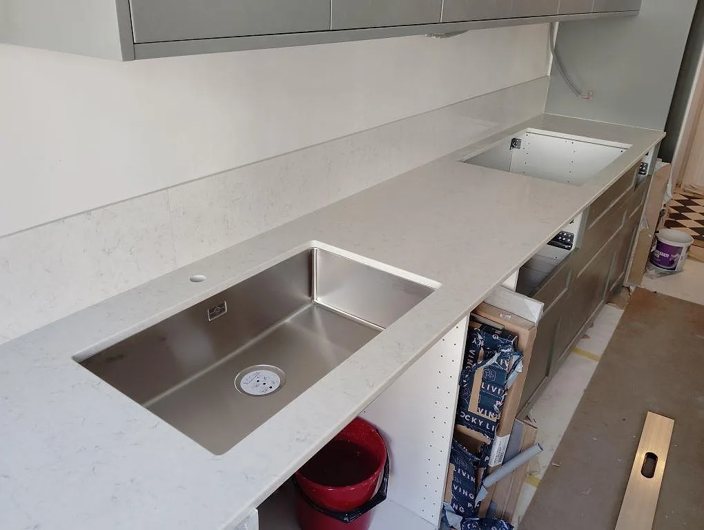 Polerad köksbänkskiva i Silestone Snowy Ibiza, ljus kvartskomposit, med underlimmad rostfri diskho, utskärning för häll och låg stänkkant i Stockholm.