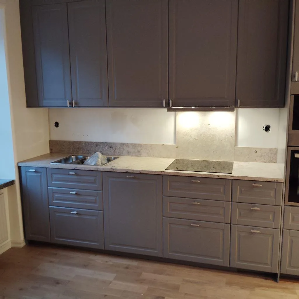 Köksbänkskiva i vit Silestone Snowy Ibiza, polerad kvartskomposit, med synlig rostfri diskho och häll i ett greige kök i Stockholm.