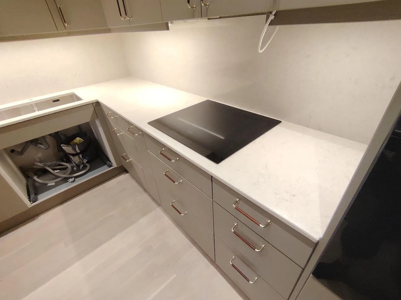 Närbild av polerad Silestone Snowy Ibiza köksbänkskiva i komposit med infälld häll, greige skåp och ljust stänkskydd i Stockholm.