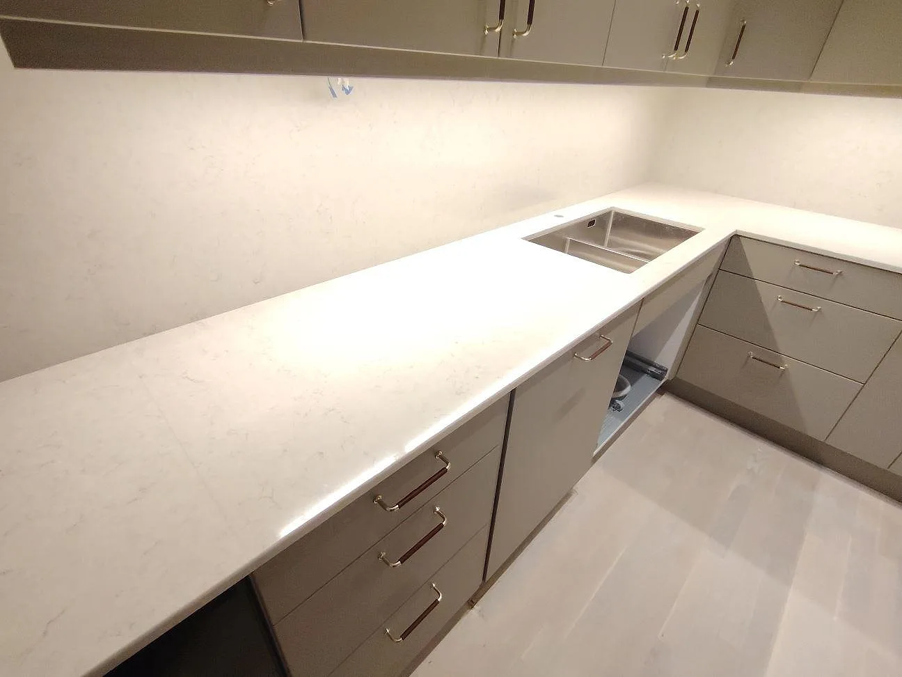 Polerad köksbänkskiva och stänkskydd i Silestone Snowy Ibiza komposit med rostfri diskho och belysning under överskåpen i Stockholm.