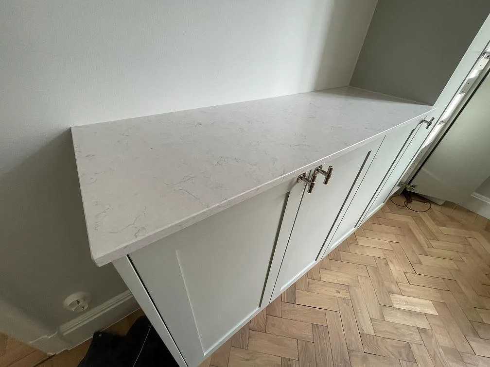 Närbild av vit polerad Silestone Snowy Ibiza kvartskomposit som bänkskiva över vita köksluckor och fiskbensparkett i Stockholm.