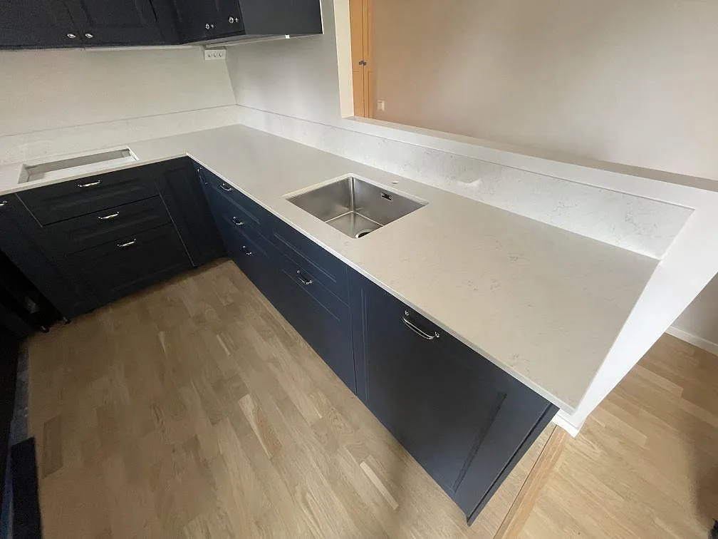 Närbild på polerad Silestone Snowy Ibiza som köksbänkskiva med rostfri diskho och uppvikt stänkskydd i Stockholm.