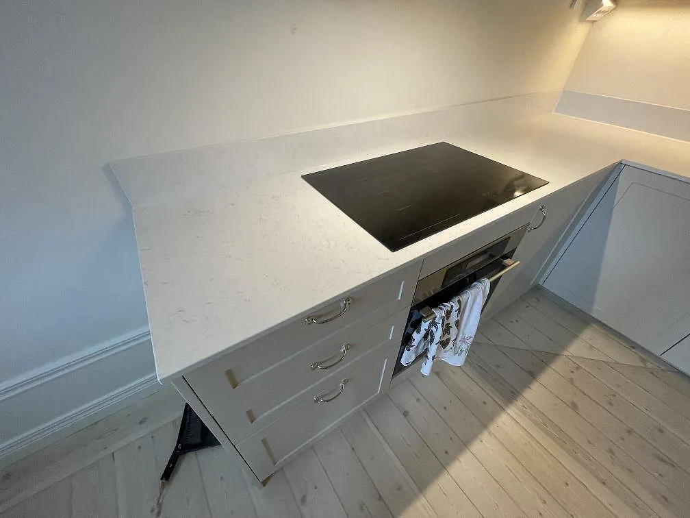 Närbild på polerad vit Silestone Snowy Ibiza kompositbänkskiva med svart infälld häll och svag ådring i ett kök i Stockholm.
