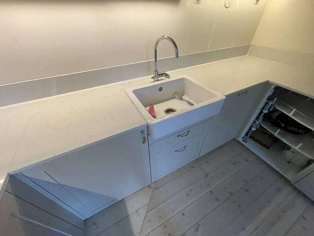 Lång bänkrad i polerad Silestone Snowy Ibiza kvartskomposit med vit diskho, öppna stommar och låg stänkkant i Stockholm.
