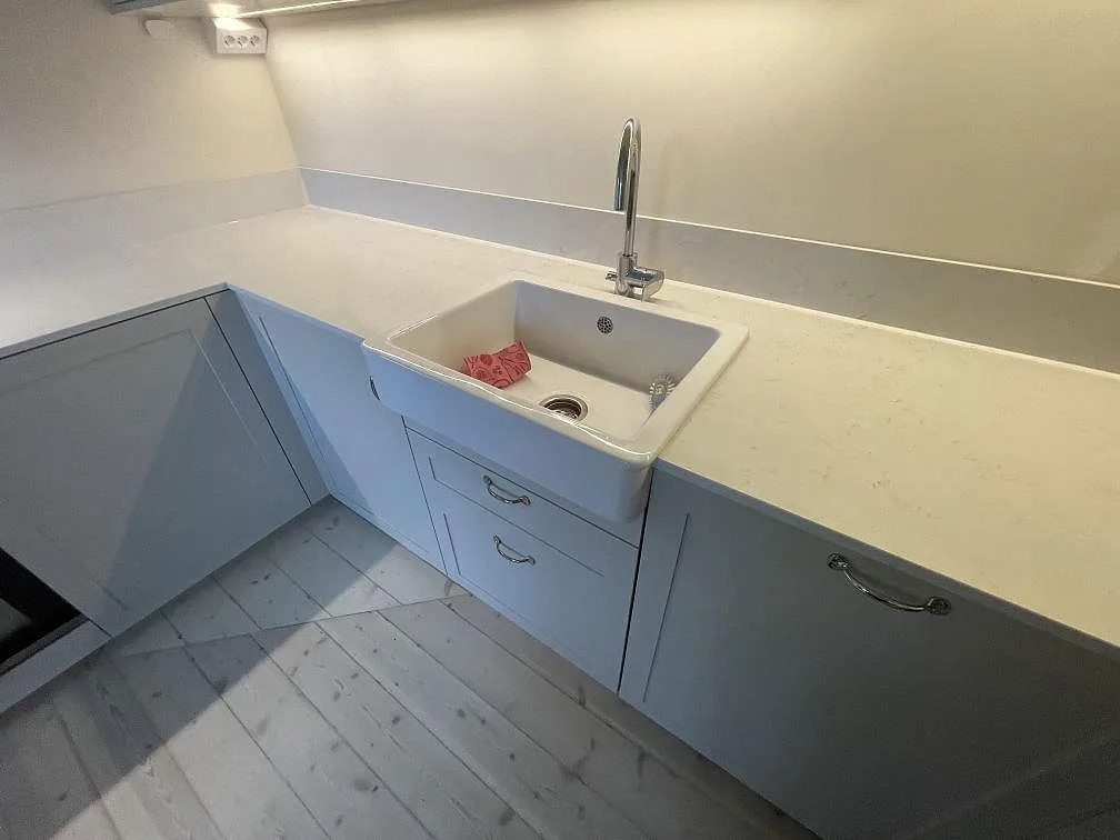 Vit diskho och kromad blandare vid en polerad Silestone Snowy Ibiza köksbänkskiva med låg stänkkant i Stockholm.