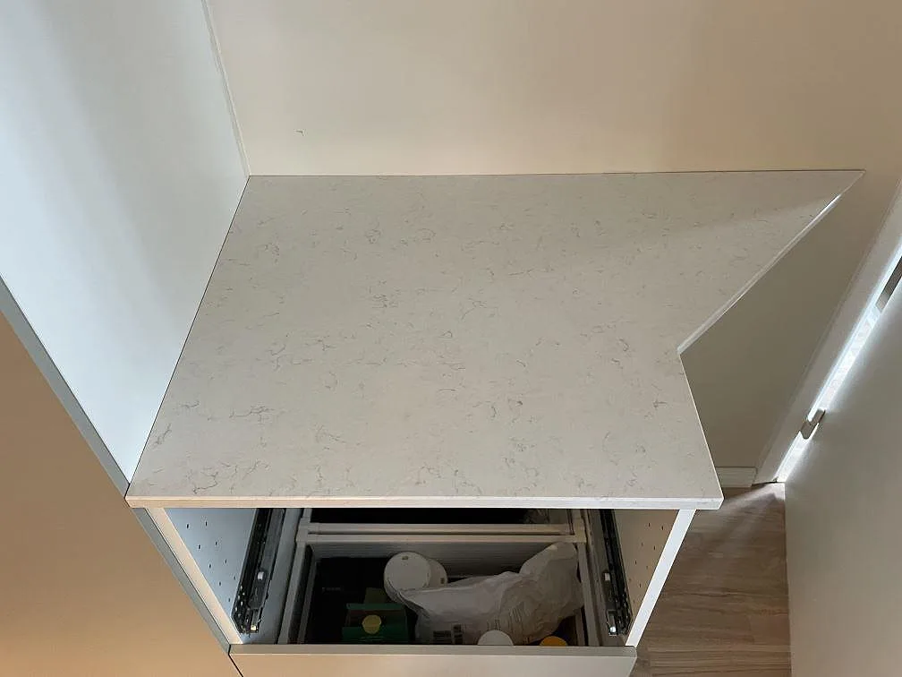 Mindre bänkdel i polerad Silestone Snowy Ibiza kvartskomposit med diskret ådring på en öppen underskåpsstomme i Stockholm.