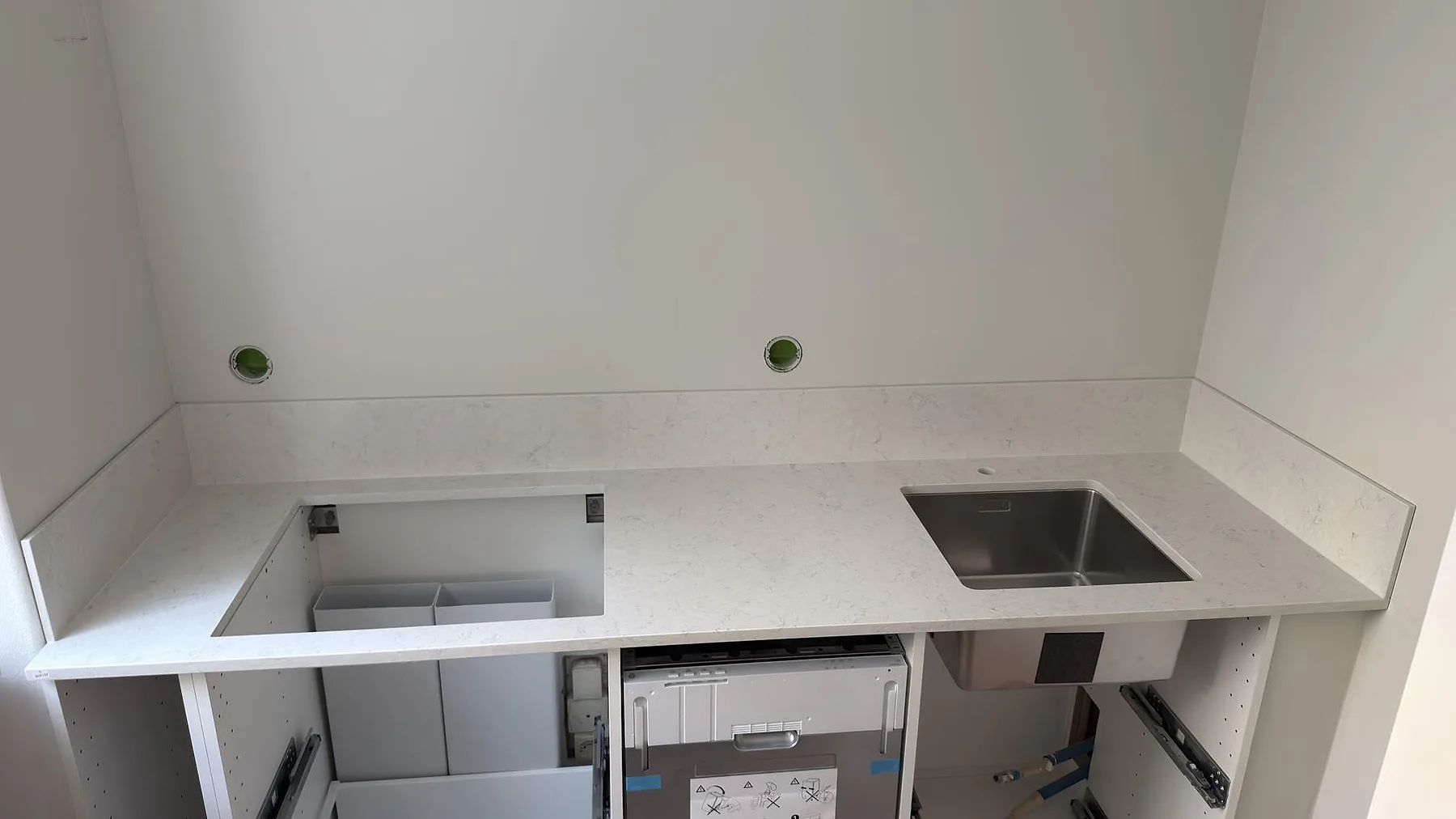 Polerad köksbänkskiva i Silestone Snowy Ibiza med låg stänkkant och rostfri diskho under montering i Stockholm.