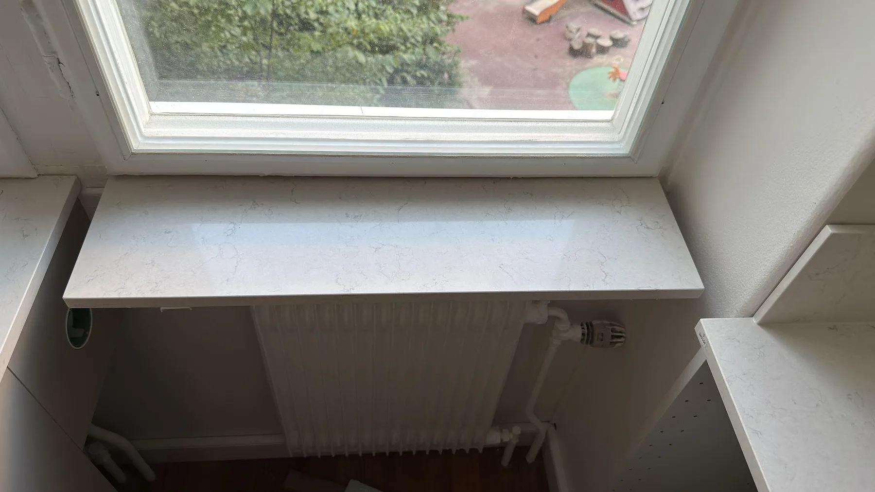 Detalj av fönsterbänk i polerad Silestone Snowy Ibiza intill köksbänken, monterad vid radiator i Stockholm.