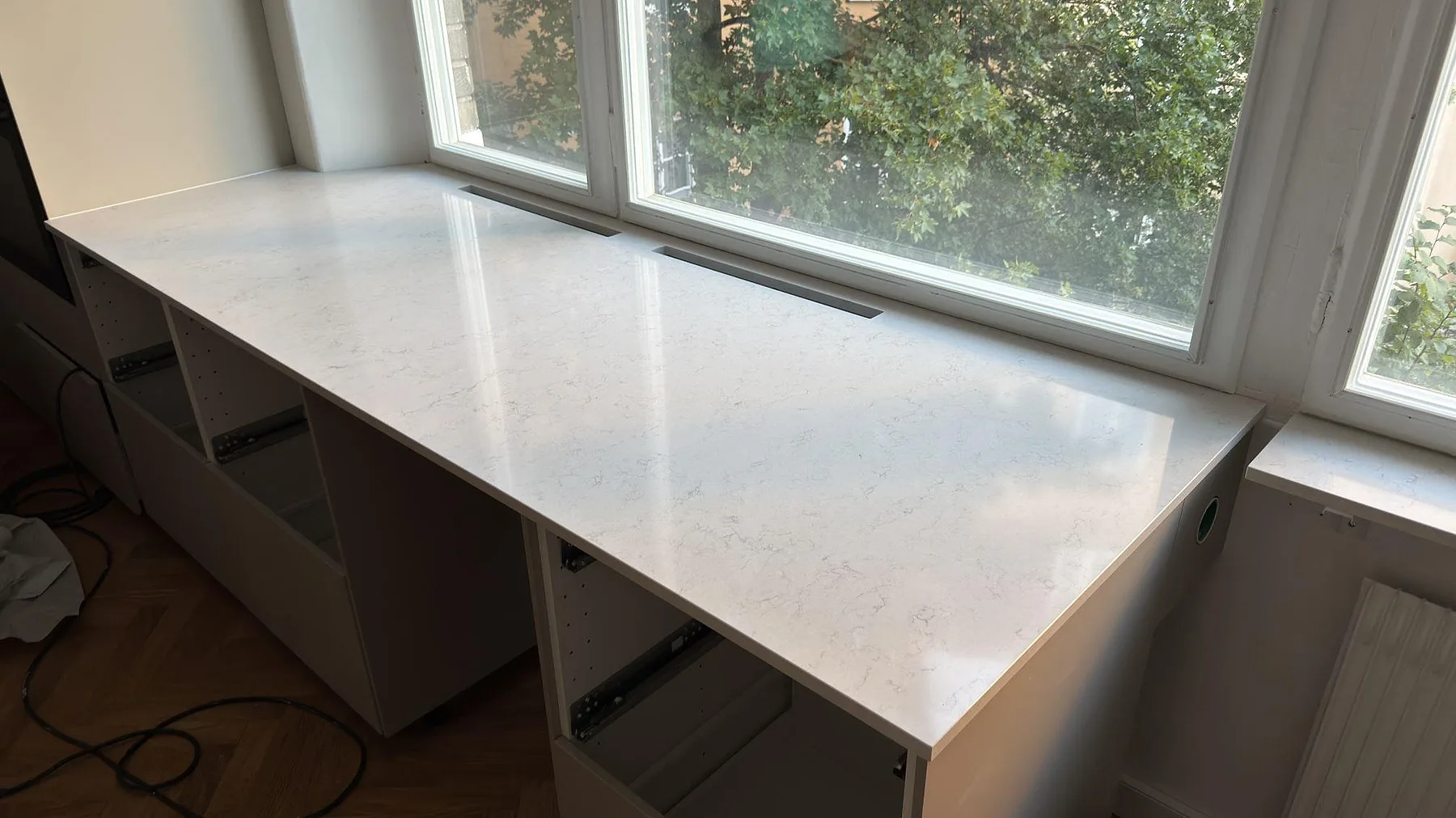 Närbild av polerad Silestone Snowy Ibiza som fönsternära köksbänk med ventilgaller och ljus ådring i Stockholm.