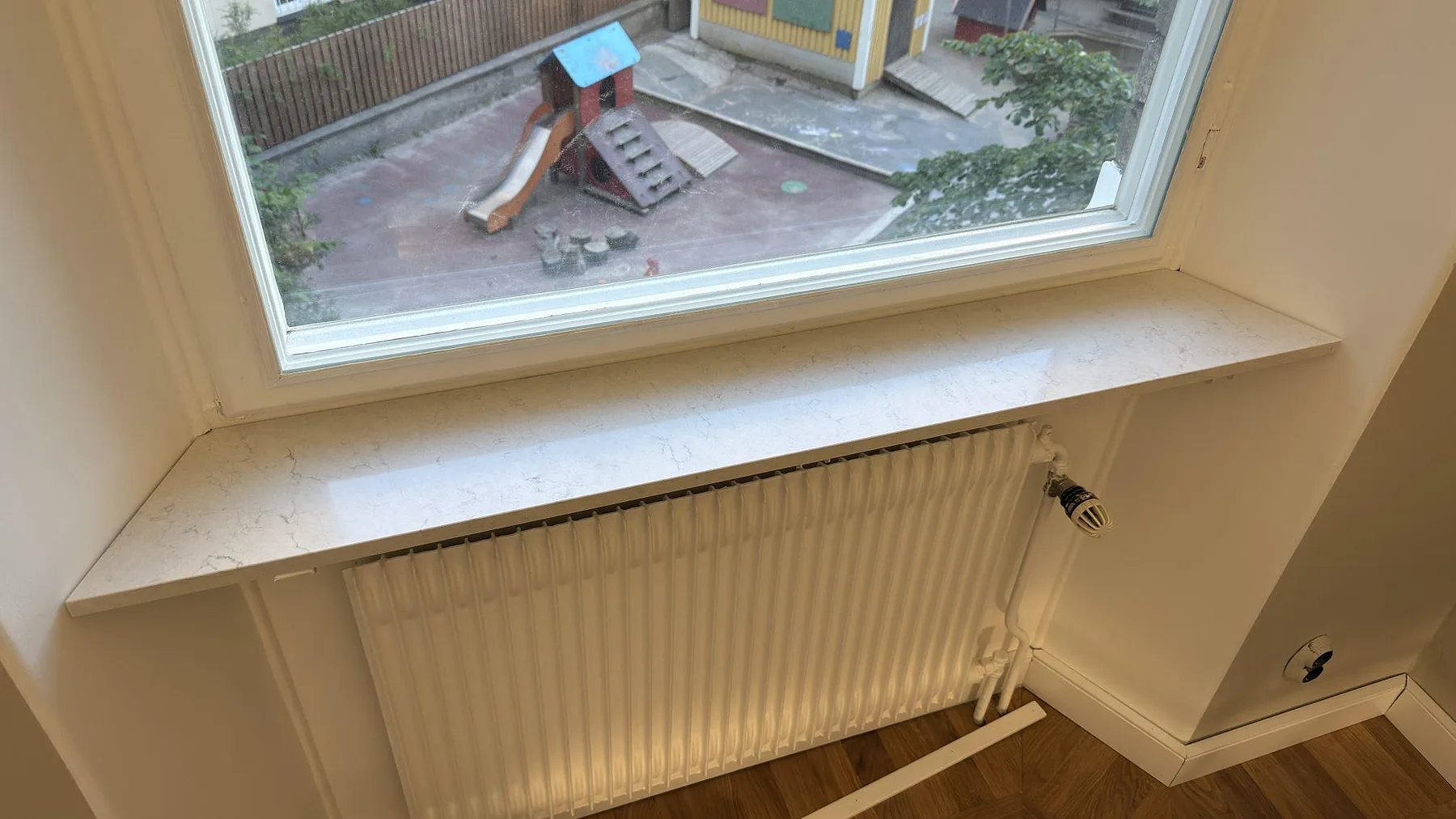 Fönsterbänk i polerad Silestone Snowy Ibiza, ljus kompositsten med grå ådring, monterad ovanför radiator i Stockholm.