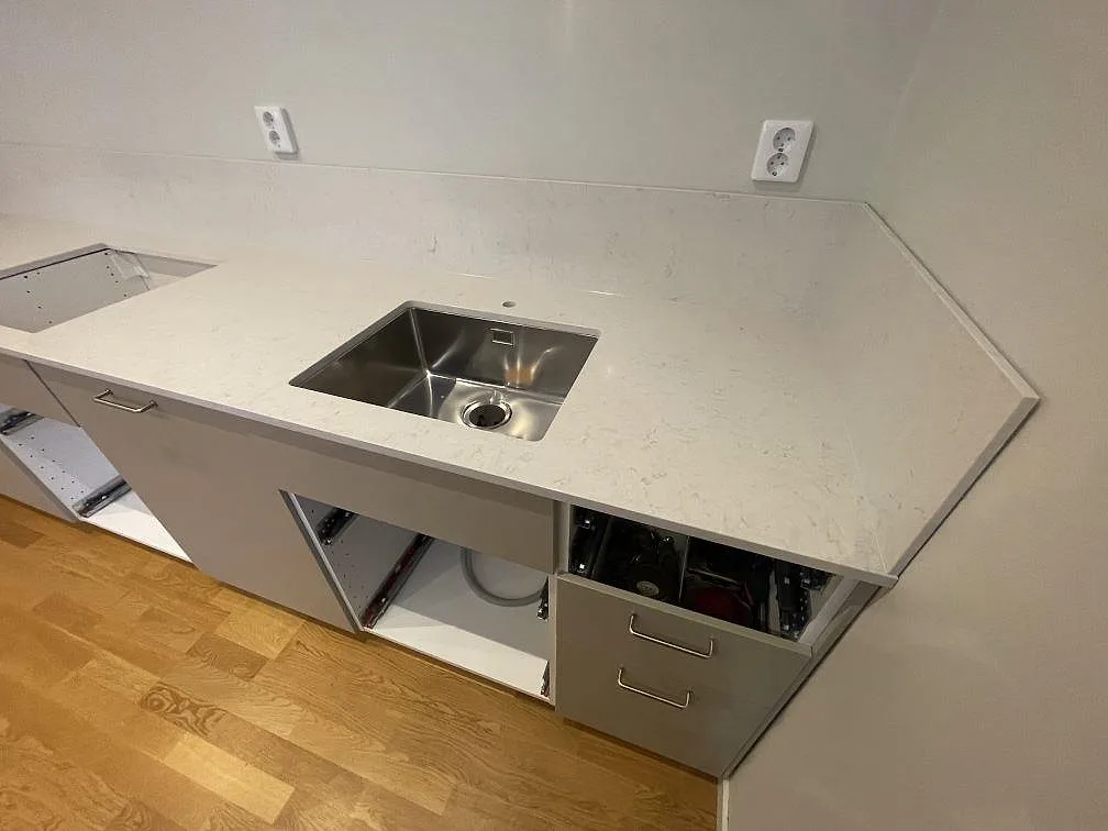 Underlimmad rostfri diskho i vit polerad Silestone Snowy Ibiza vid ett vinklat bänkhörn i ett kök i Stockholm.