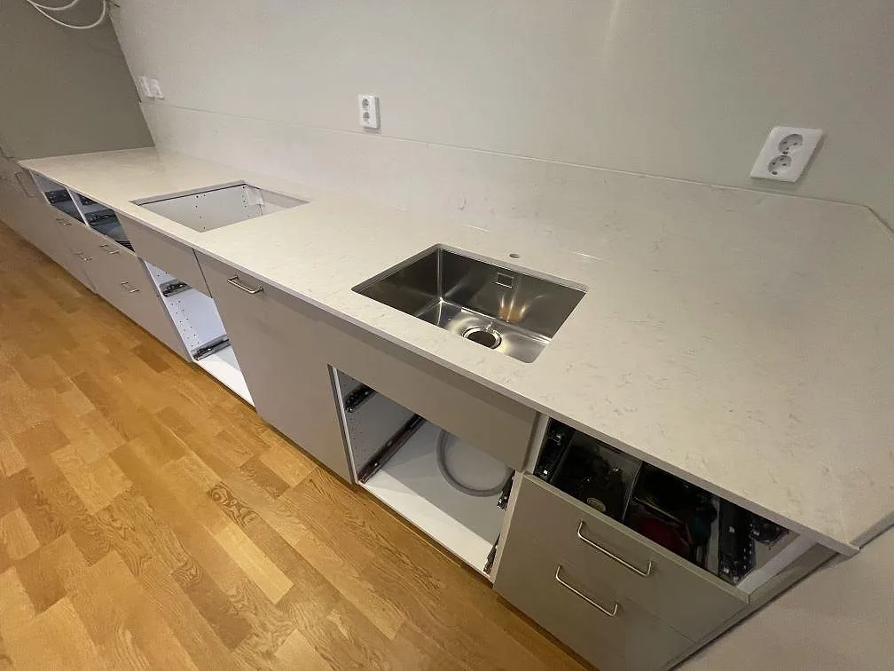 Lång köksbänkskiva i vit Silestone Snowy Ibiza, polerad, med två diskhopositioner och vinklat hörn i ett kök under montering i Stockholm.