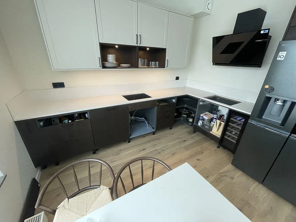 Polerad köksbänkskiva i ljus Silestone Snowy Ibiza som löper i L-form längs två väggar med mörka skåp och vinkyl i ett kök i Stockholm.