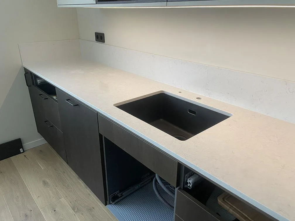 Underlimmad mörk diskho i en polerad köksbänkskiva av Silestone Snowy Ibiza med borrat blandarhål och lågt uppvikt stänkskydd i Stockholm.